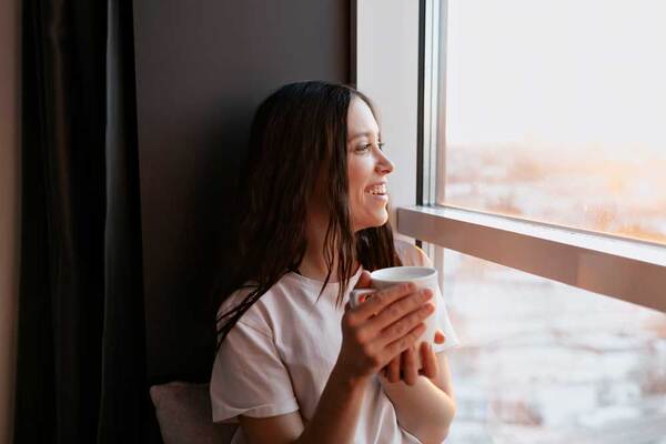 Adult holding a mug near a window, taking a quiet breath